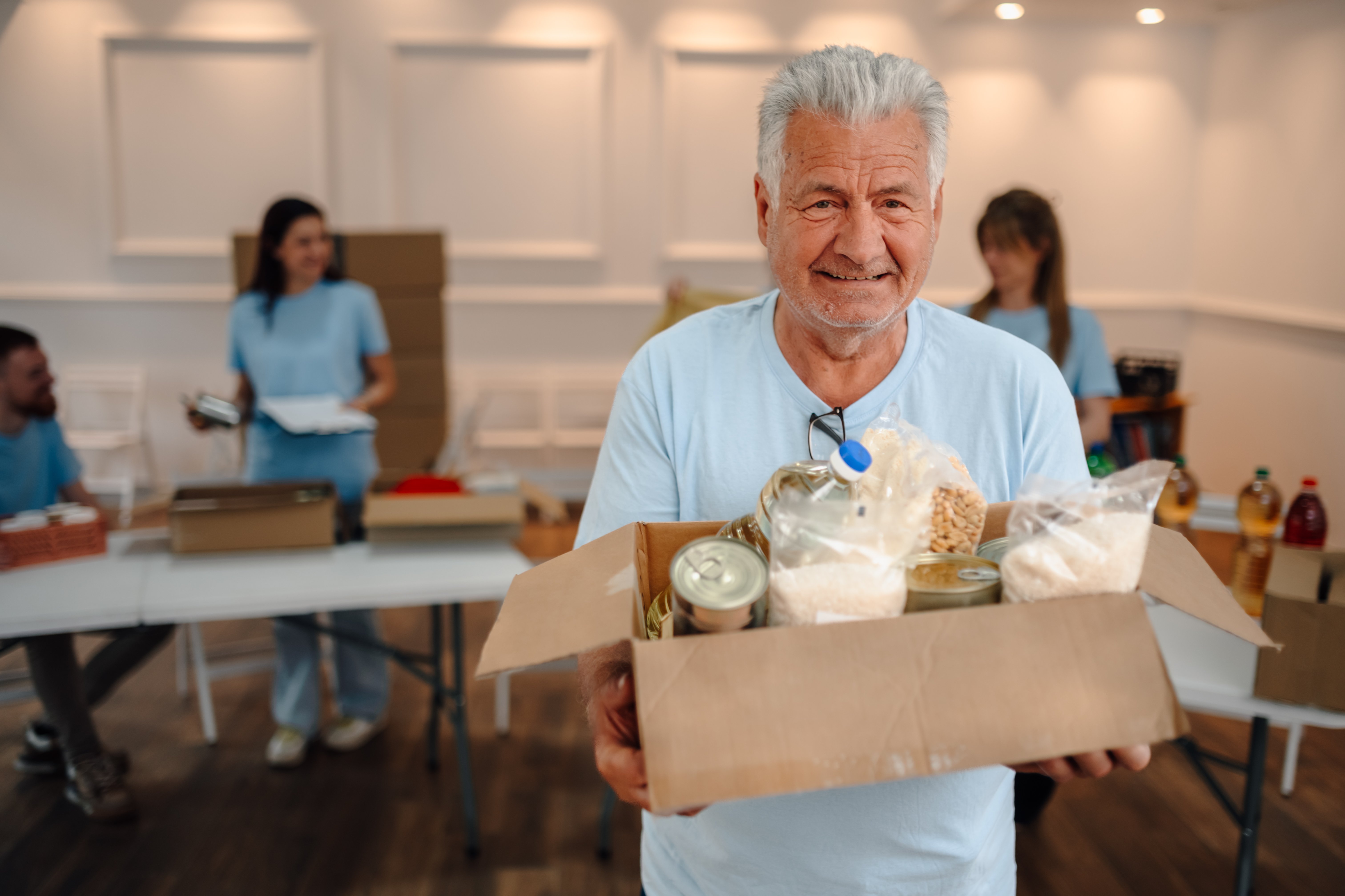 Senior man smiling, holding a box of groceries for a food bank, participating in a social community service event