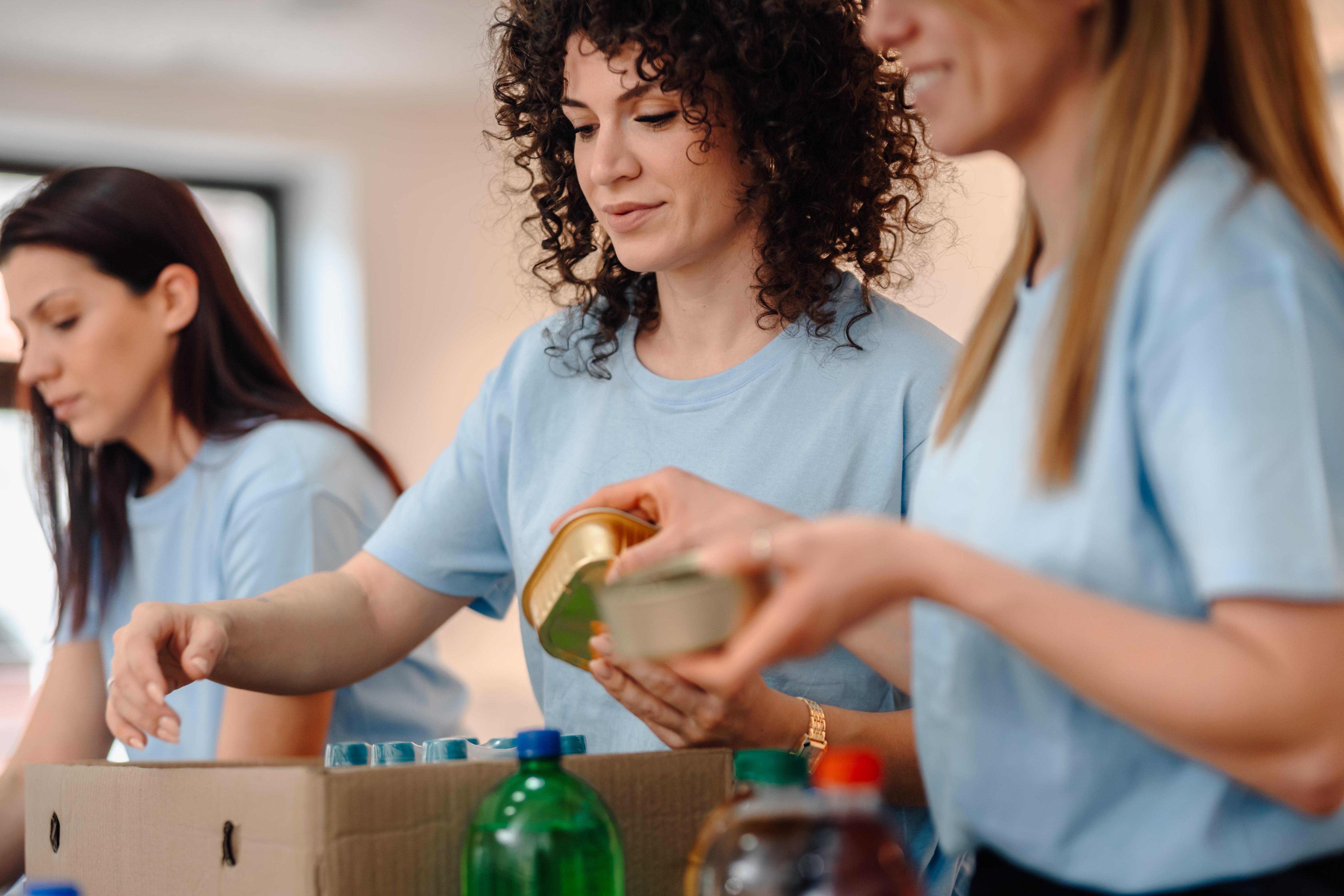 Group of women volunteers working together, sorting donated food items and beverages into boxes for distribution to the community